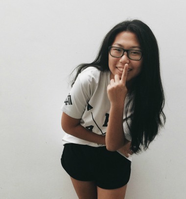 black haired girl smiling brightly with a finger on top of her nose
